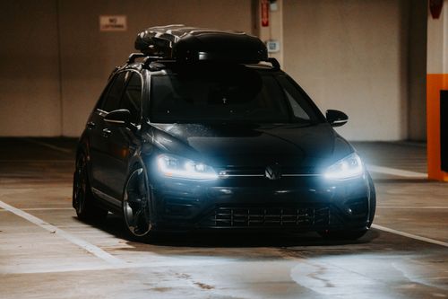 Free A stylish black car with headlights on, parked indoors in a dimly lit garage, exuding elegance. Stock Photo