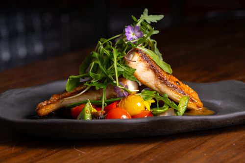 Free Delicious gourmet dish featuring grilled fish, cherry tomatoes, and arugula elegantly plated. Stock Photo