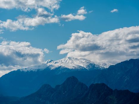 Stunning snow-covered mountain peaks under a bright blue sky with fluffy clouds.