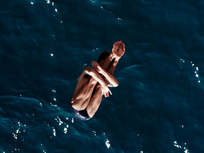 High-angle shot of a man diving into the sea, capturing dynamic motion and excitement.