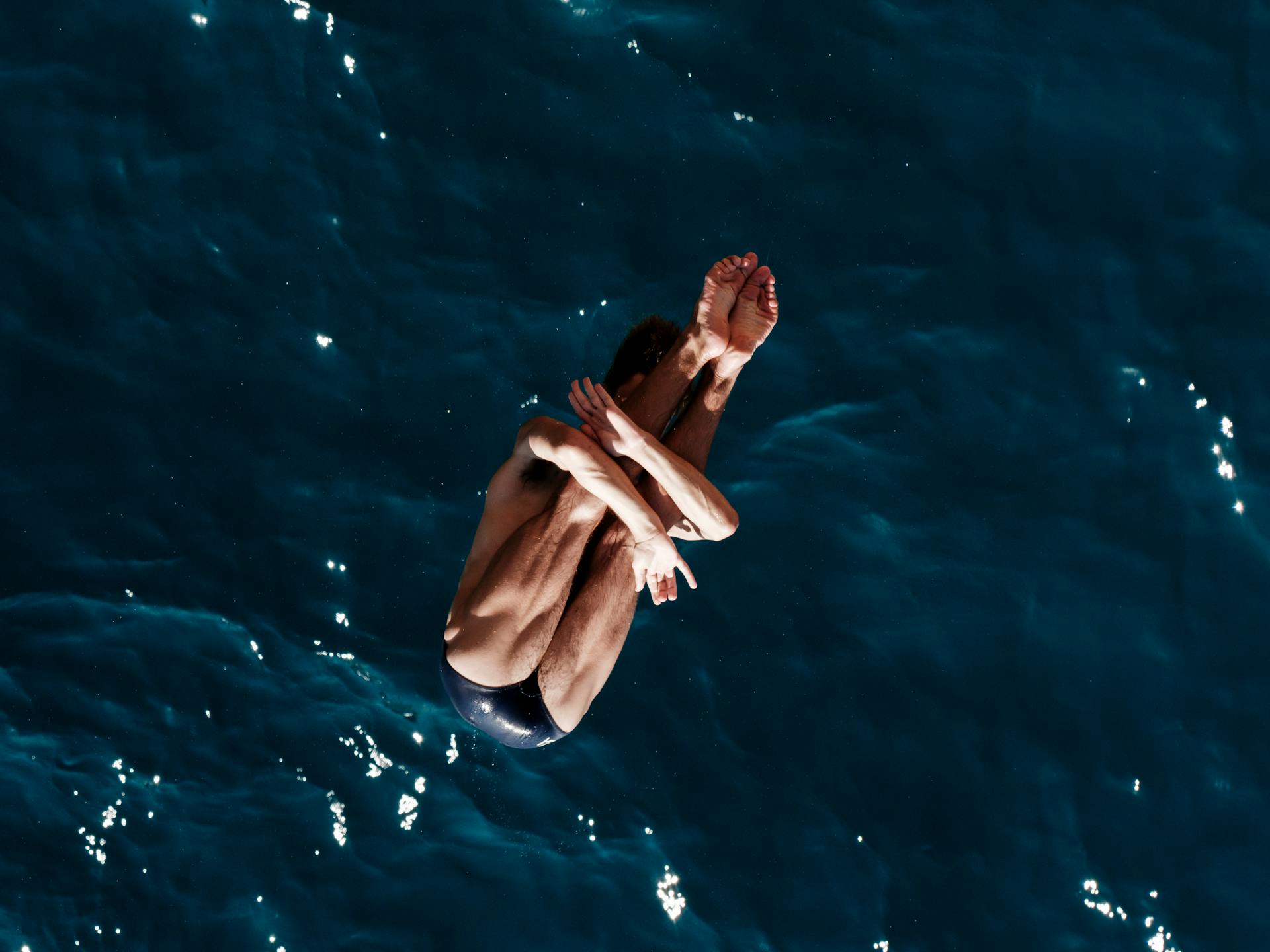 a professional male diver is jumping off a cliff into the sea