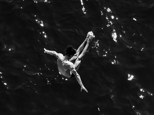 Free A dramatic black and white shot of a person diving into the shimmering sea, capturing motion and bravery. Stock Photo