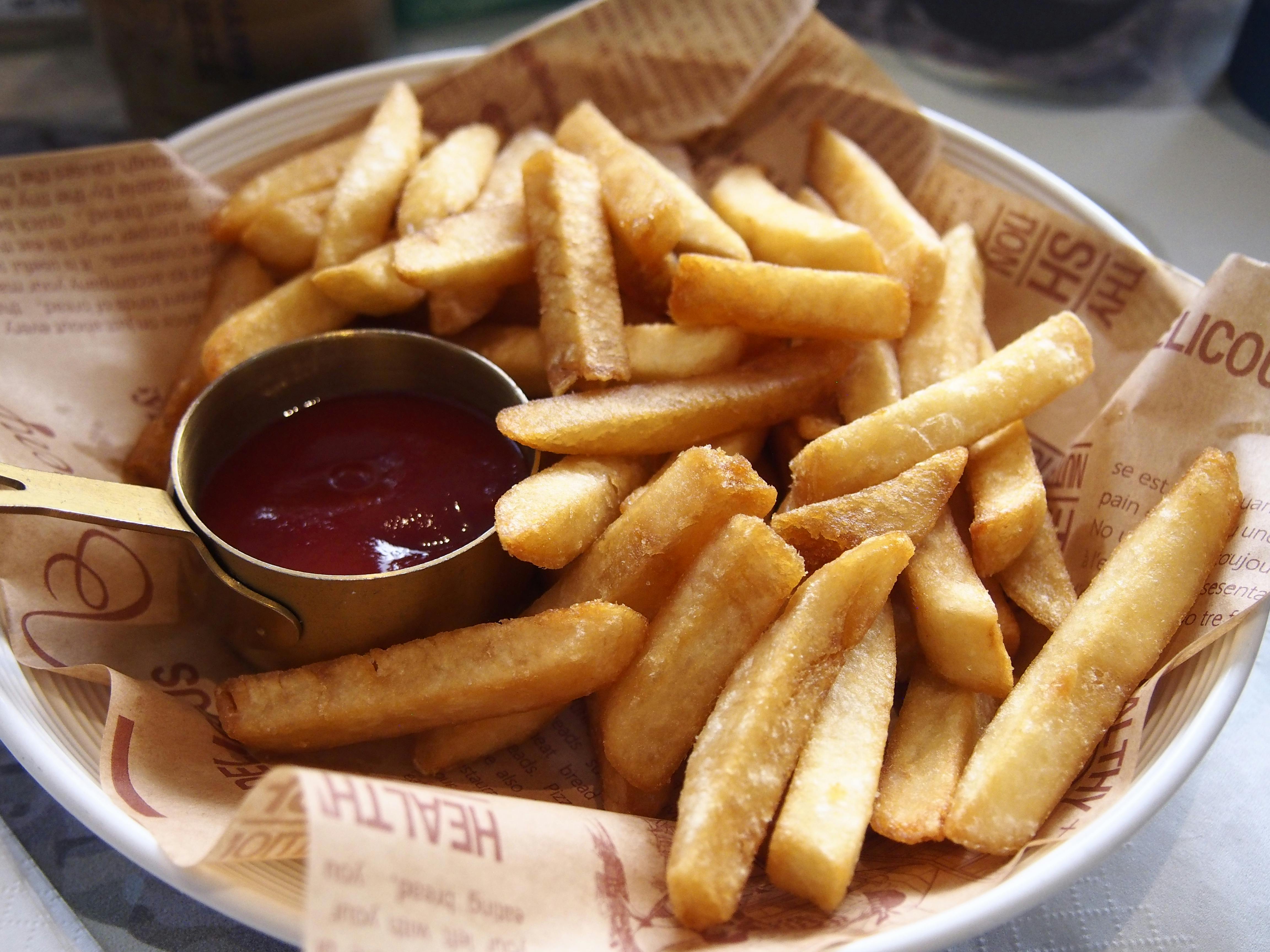 A plate of golden, crispy French fries served with a side of ketchup.