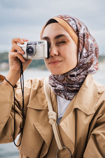 Young woman in a patterned hijab taking a photo with a vintage camera outdoors in Istanbul.