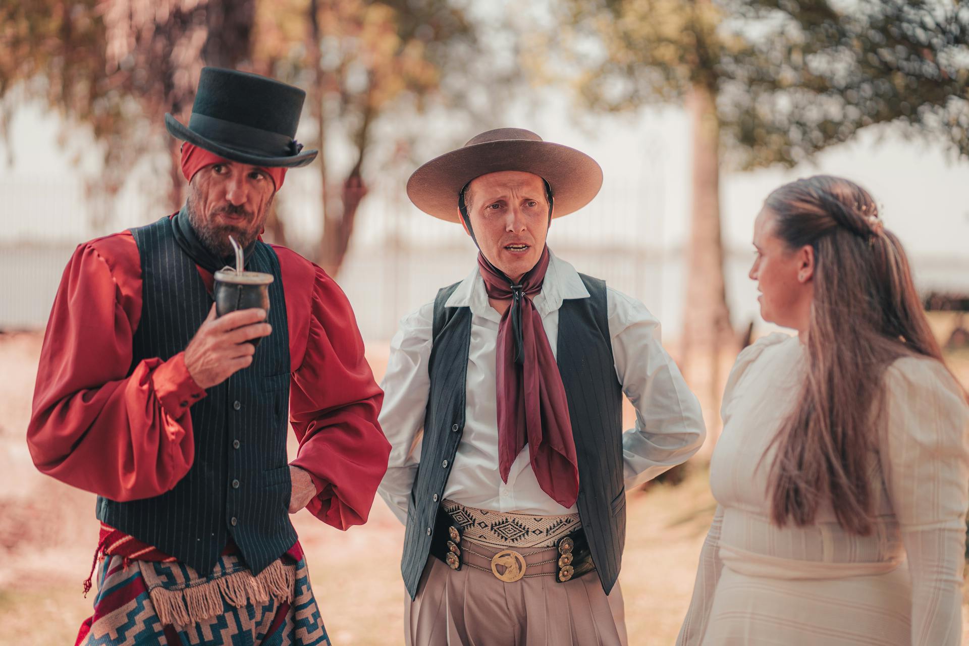 Drie volwassenen in traditionele Zuid-Amerikaanse gaucho kleding die buiten een gesprek voeren.