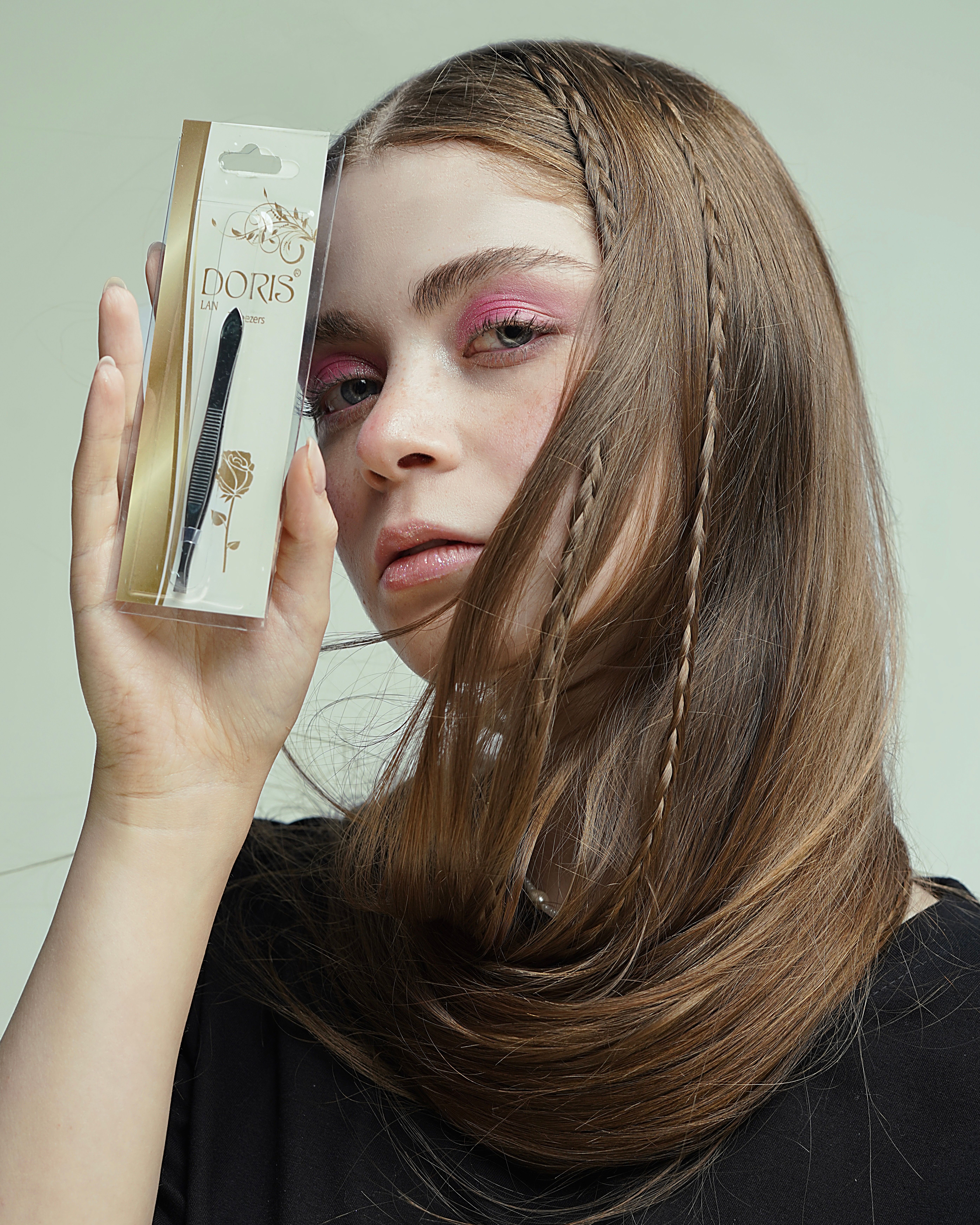 A young woman holds a Doris eyeliner package close to her face, showcasing modern cosmetic style.