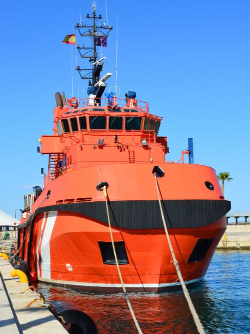 Free A brightly colored red tugboat docked on a sunny day, showcasing nautical elements. Stock Photo