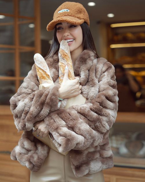 Free Woman in luxurious coat holds baguettes outside a bakery, smiling warmly. Stock Photo