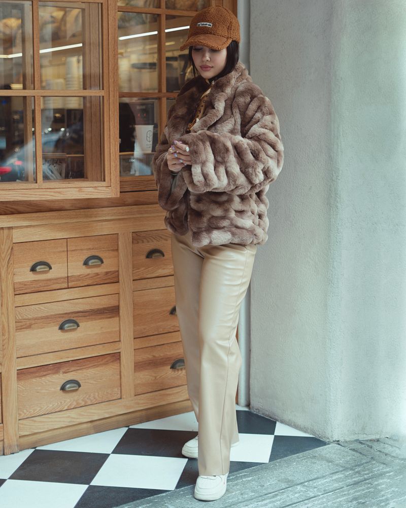 Woman in faux fur coat and cap posing outdoors