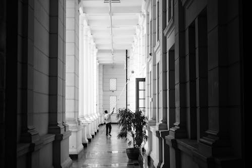 Grayscale Photo of Person Walking on Corridor