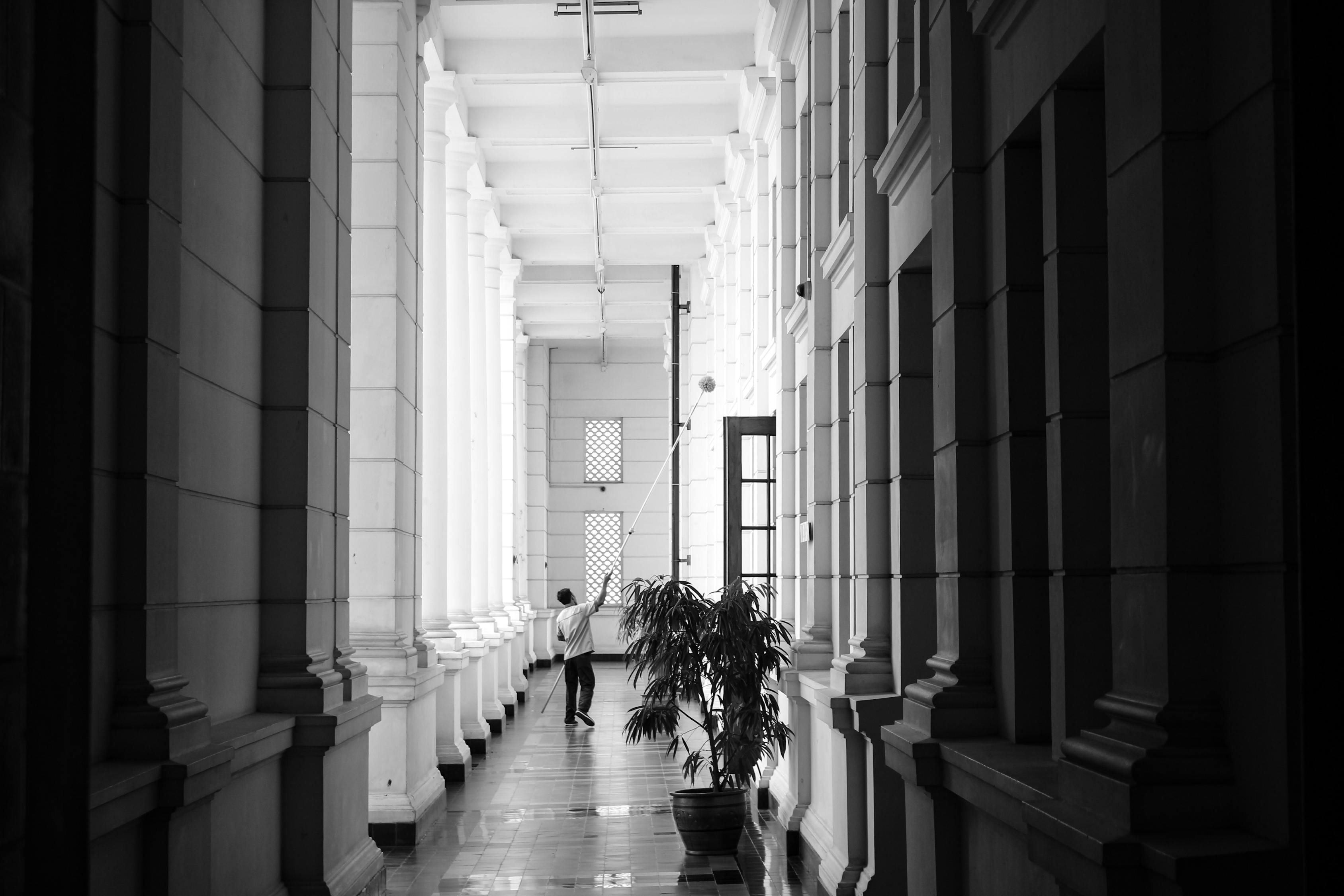 Grayscale Photo of Person Walking on Corridor