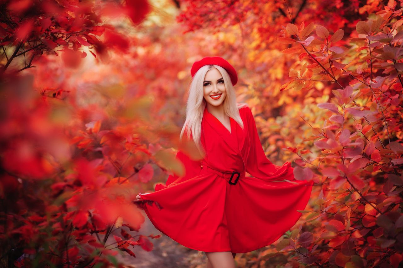 a smiling woman in a vivid red dress surrounded by lush autumn foliage