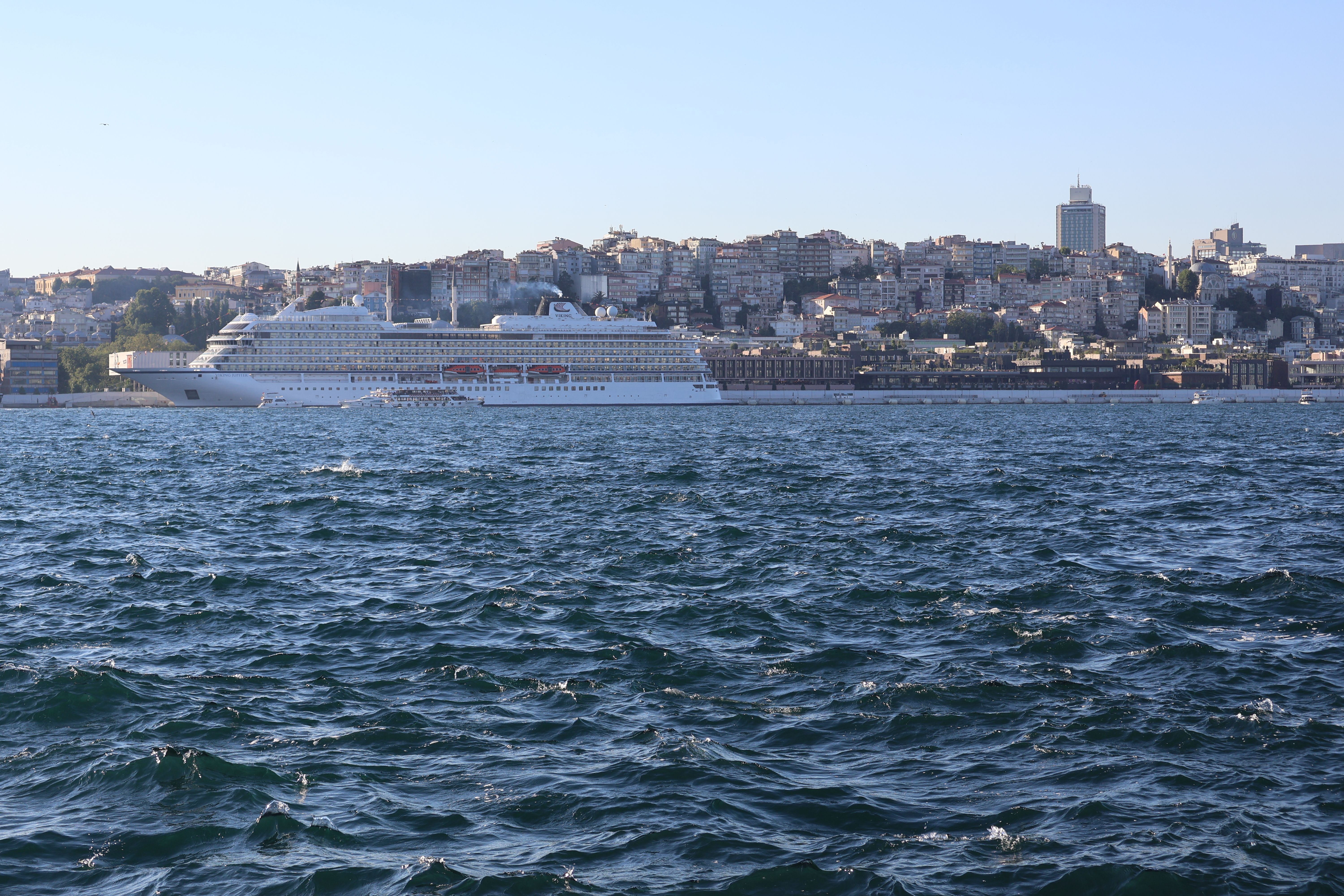 A cruise ship sails through the Bosphorus with Istanbul's skyline in the background.