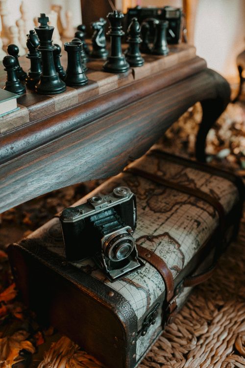 Free A vintage camera on a suitcase beside a chessboard set on a rustic wooden table. Stock Photo