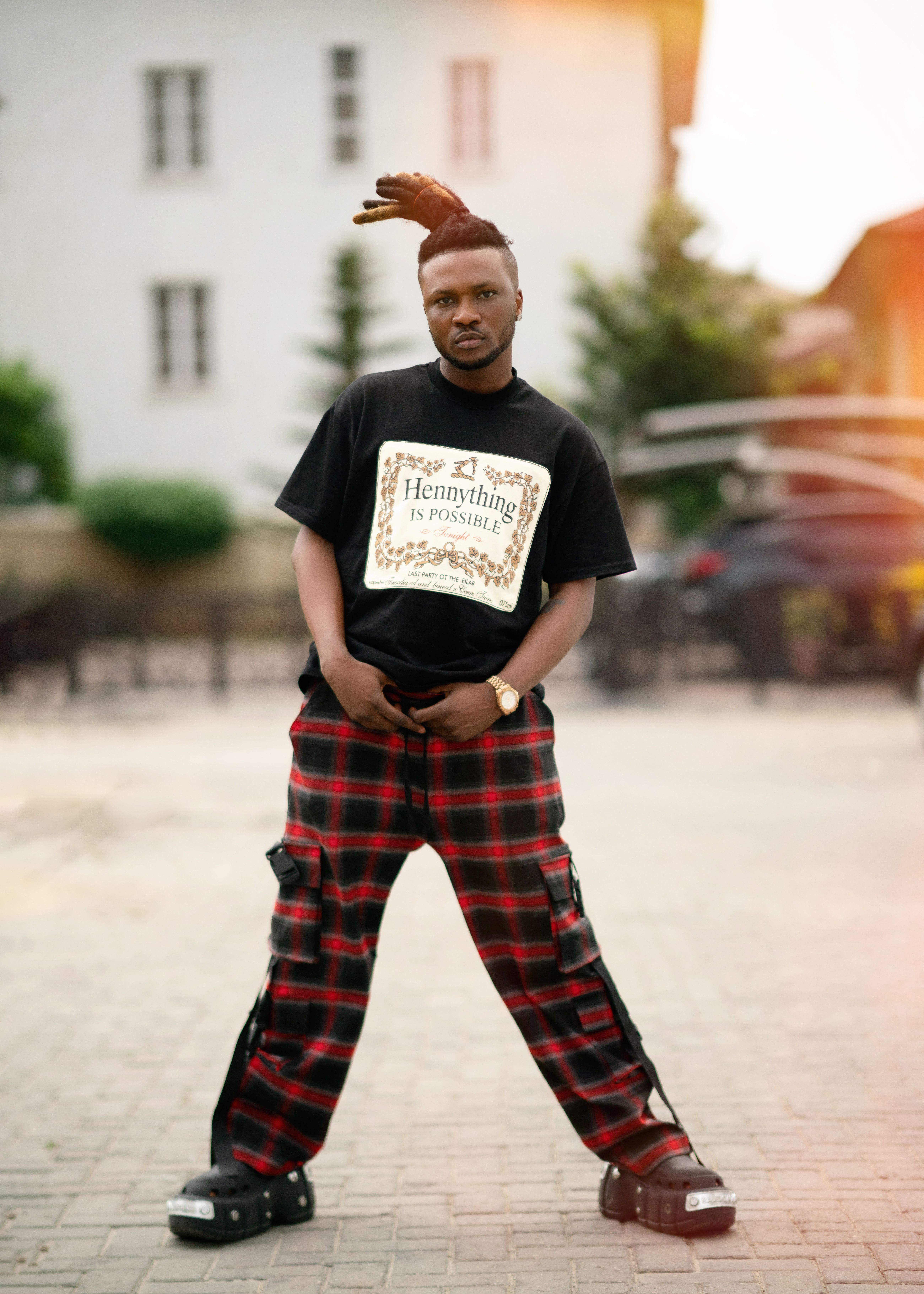 Man in urban outfit with slogan shirt and plaid pants outdoors.