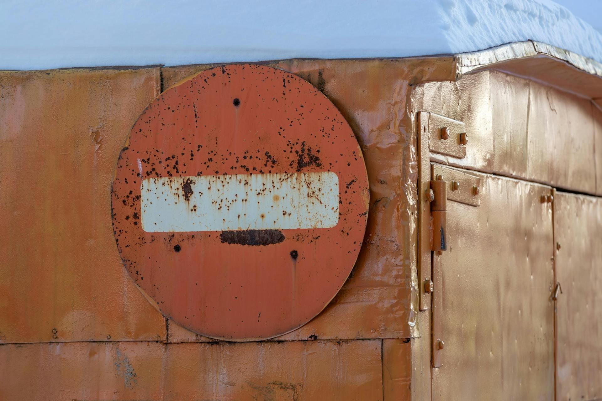 Close-up of a rusted metal container featuring a weathered circular sign.