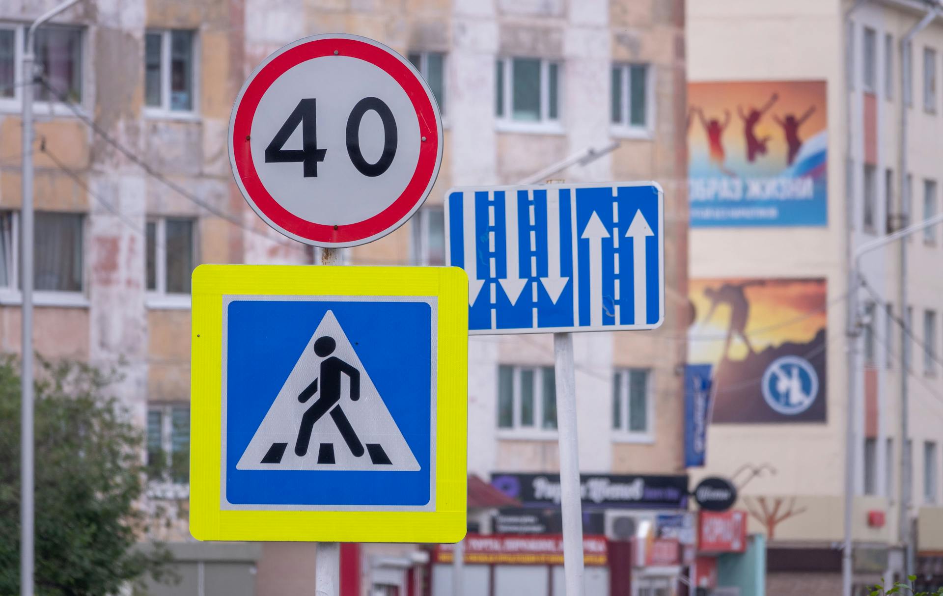 Urban street signs indicating speed limit and pedestrian crossing in a city setting.