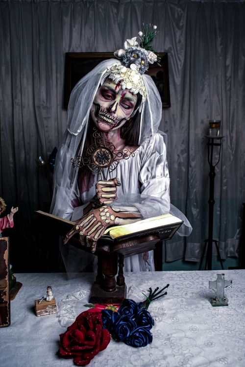 Free Halloween-inspired skeleton bride with book and roses indoors. Dark and artistic vibe. Stock Photo