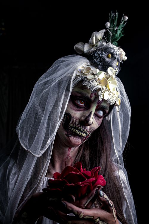 Free Dark and mysterious bride with skull makeup and veil holding a red rose against a black backdrop. Stock Photo