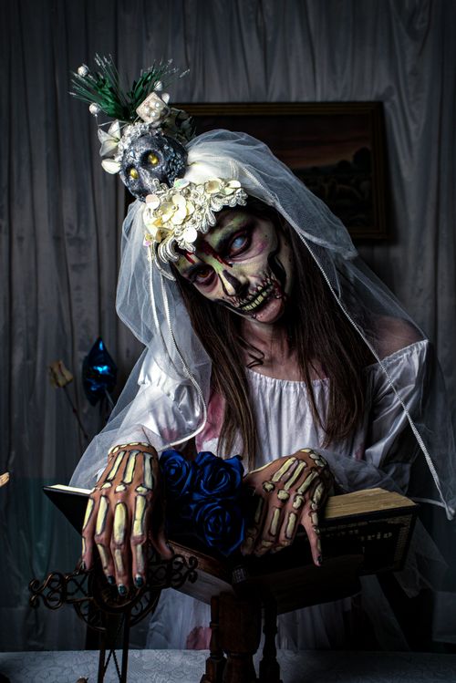 Free A haunting image of a woman in a skeleton bride costume with spooky makeup reading a book. Stock Photo