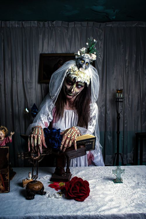Free Day of the Dead bride in skeletal makeup with altar setup indoors. Stock Photo