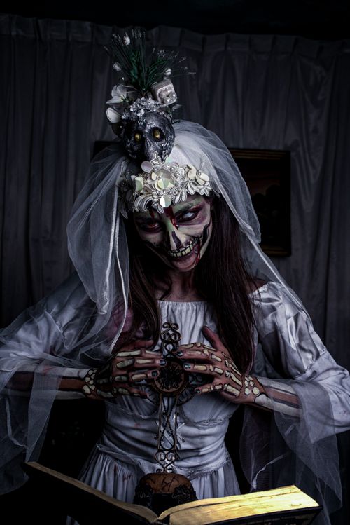 Free A haunting bride with skeleton makeup and veil reading a mysterious book in dim lighting. Stock Photo