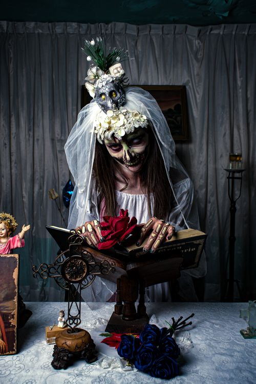 Free Woman in skeleton makeup with floral headpiece reading a book indoors. Stock Photo