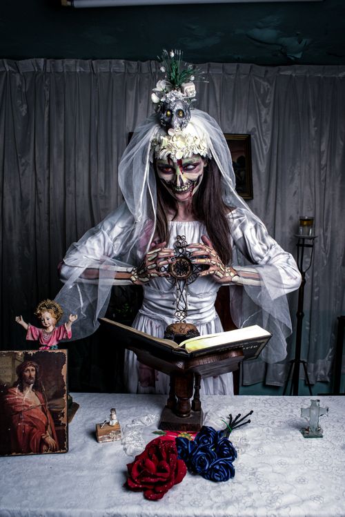 Free Skeleton bride in gothic attire performing a ritual with religious icons and flowers. Stock Photo