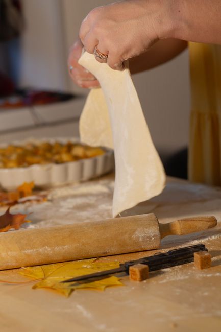 Hands stretching and rolling out pie dough on wooden surface