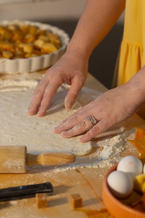 Free Close-up of hands rolling pie dough with ingredients on a wooden table. Stock Photo