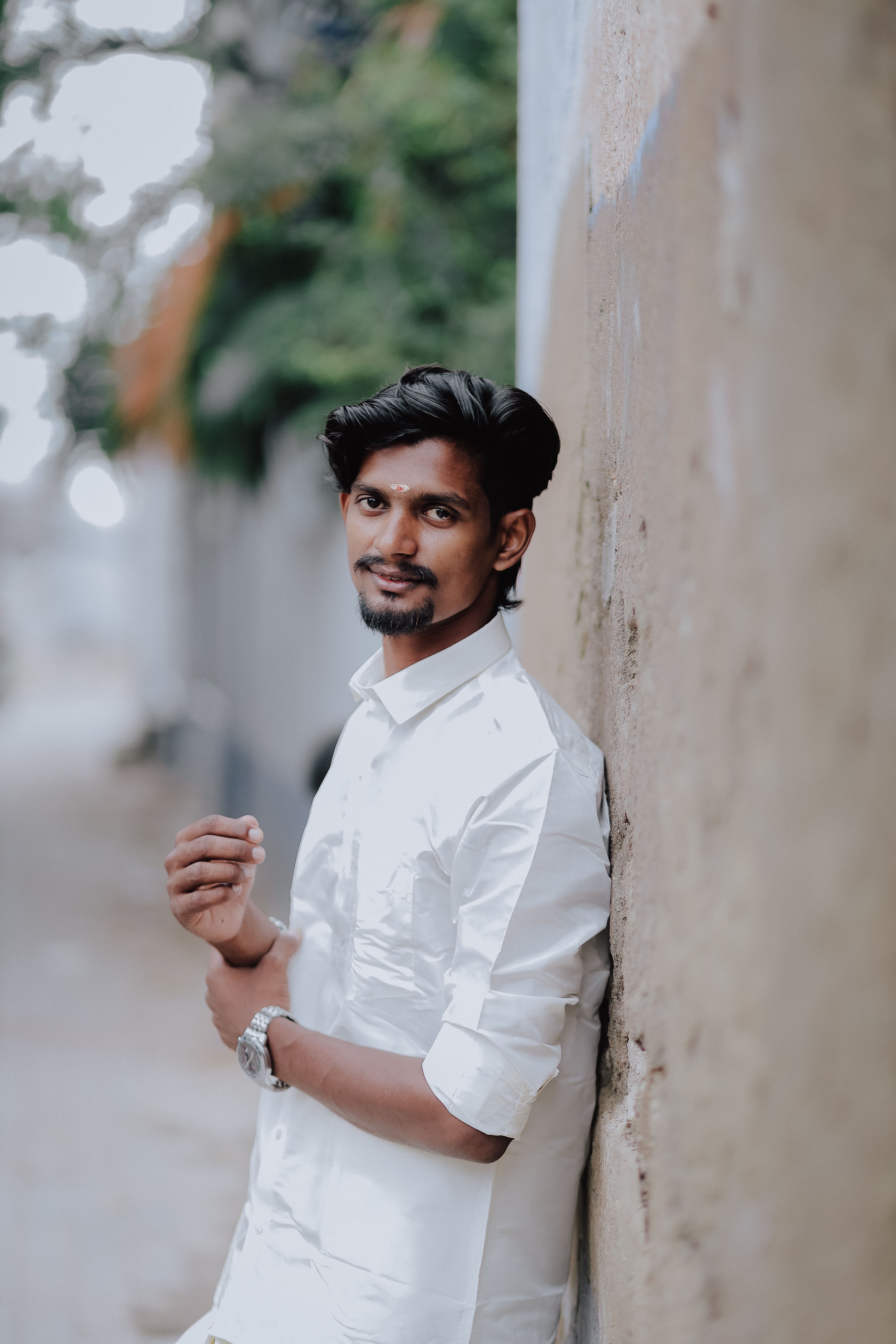 Casual portrait of a young South Asian man leaning against a wall outdoors.