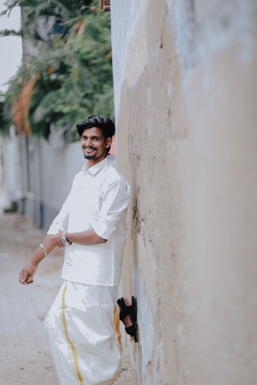 Free A smiling Indian man wearing traditional attire leaning against a wall outdoors. Stock Photo