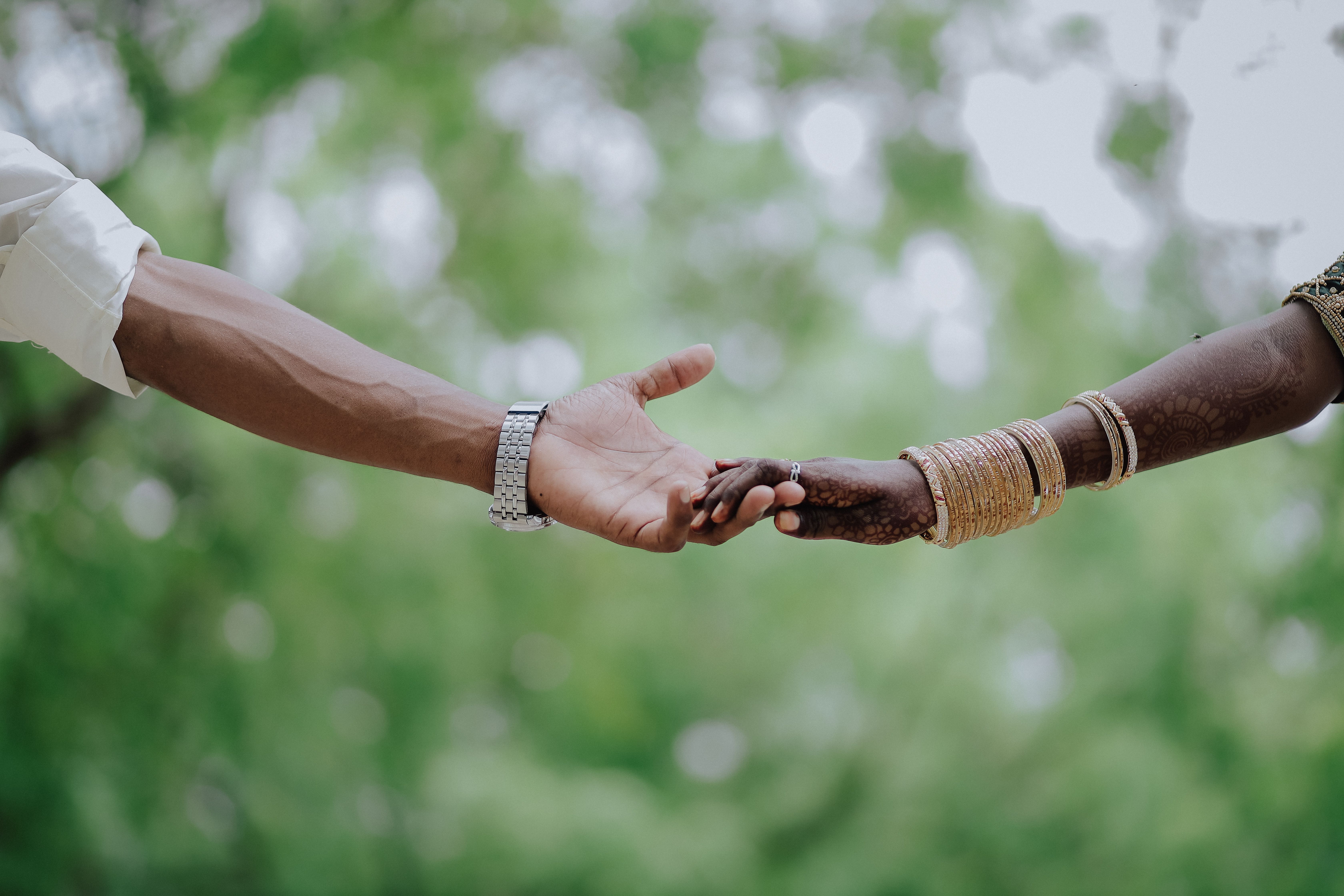 Beautiful capture of an Indian couple's hands embracing in a traditional wedding setting outdoors.