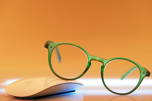 Stylish green eyeglasses with a white computer mouse on a warm orange backdrop.