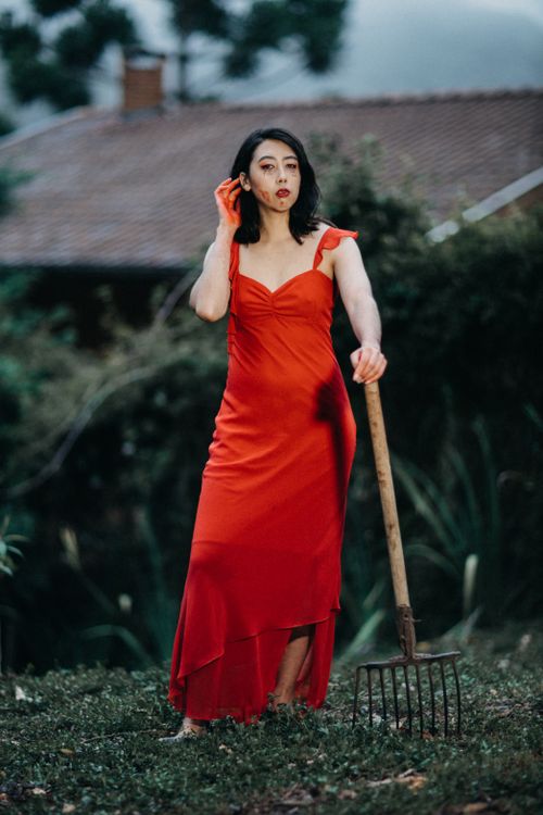 Free A stylish woman in a red dress poses with a pitchfork in a garden setting. Stock Photo