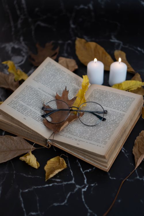 Free An open vintage book with glasses and candles, decorated with autumn leaves on a dark marble background. Stock Photo