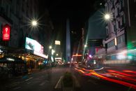 Long-exposure night shot of the Obelisk in Buenos Aires with colorful light trails on a bustling street.