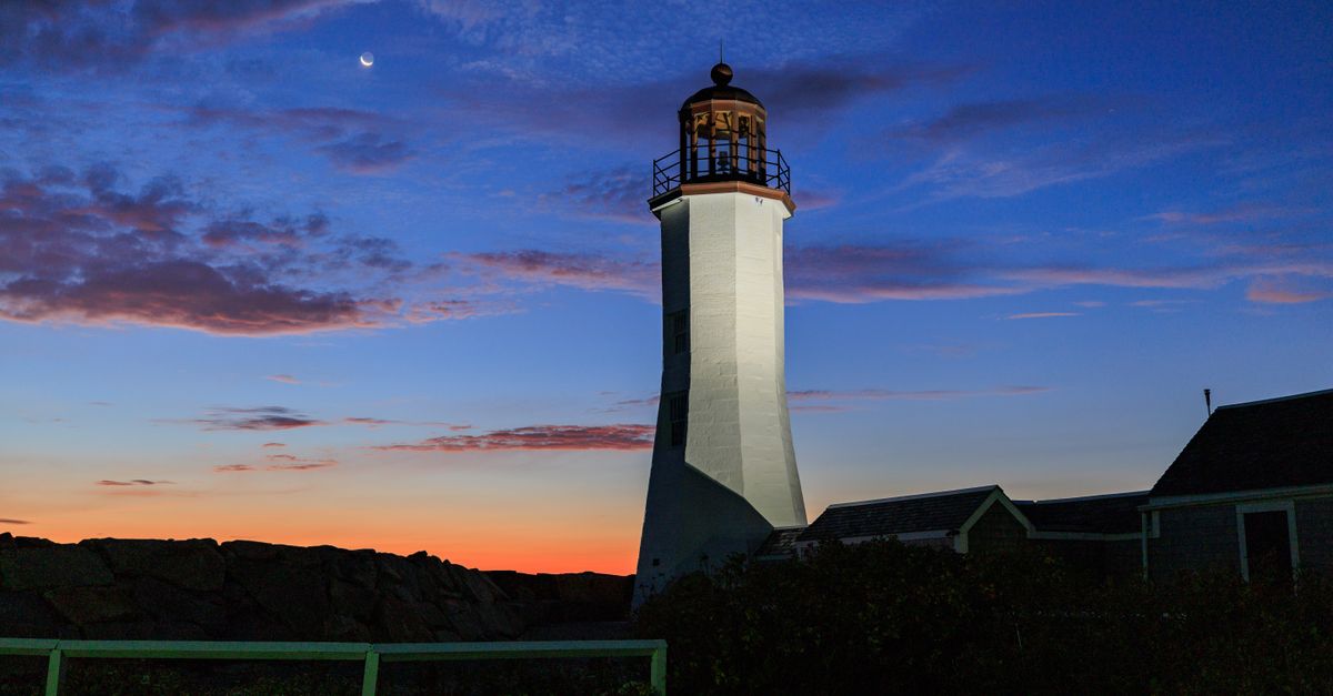 Scituate lighthouse silhouetted against a stunning twilight sky with crescent moon.