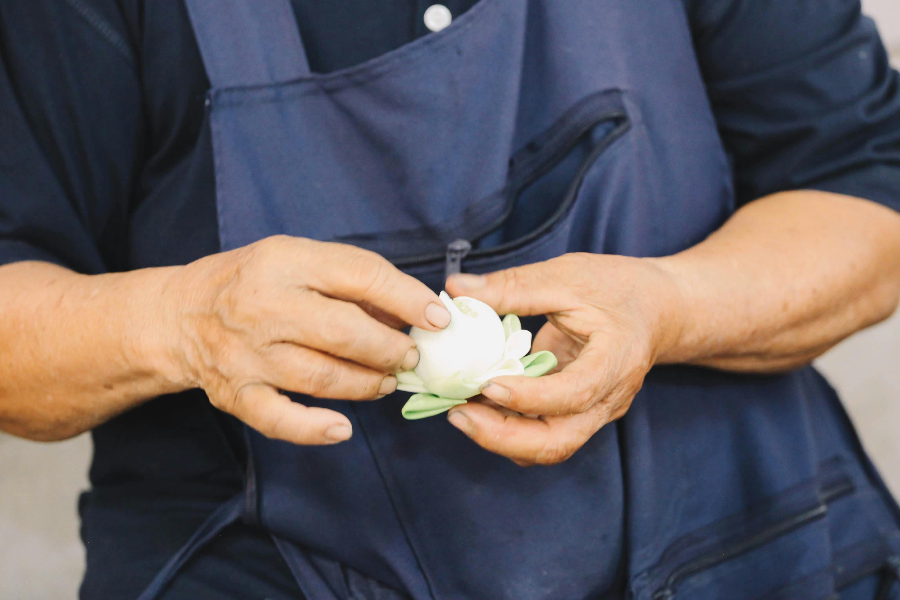 Close-up of hands meticulously crafting a lotus flower in a Bangkok market setting.