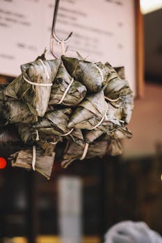 Close-up of traditional Asian street food wrapped in banana leaves in a bustling Bangkok market.