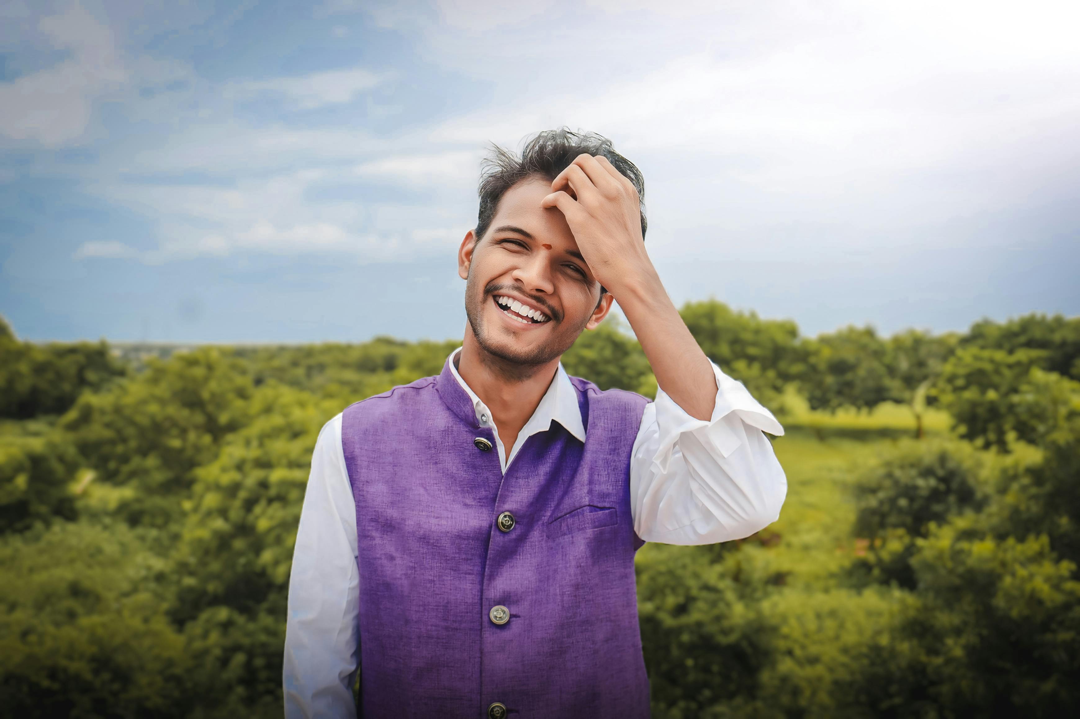 Portrait of a young man in vibrant attire, smiling against a lush green backdrop and beautiful sky.