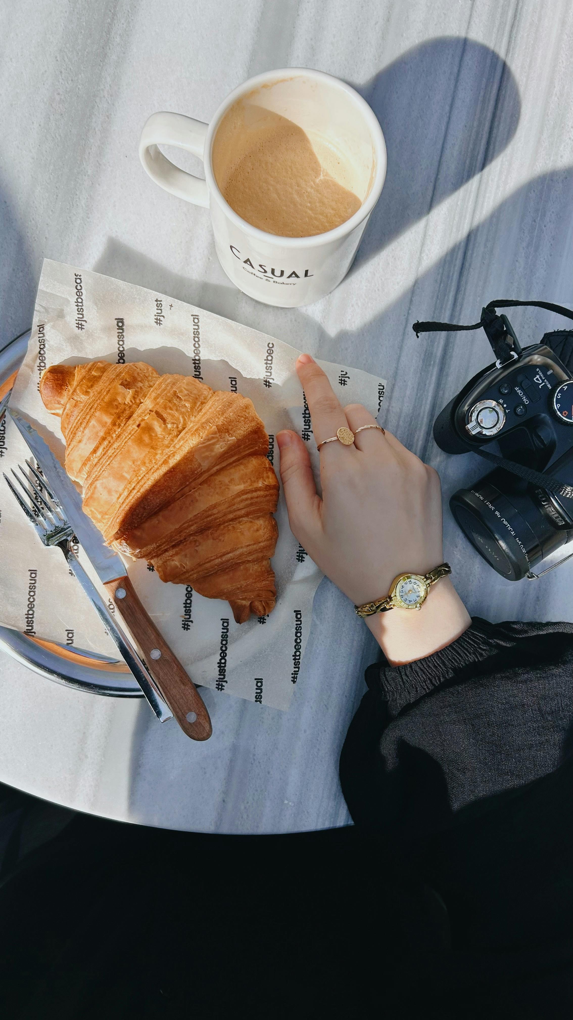 Chic breakfast setup with croissant, coffee, and vintage camera on a sunny day.