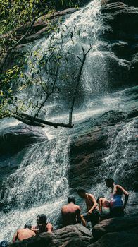 Group of people relaxing by a waterfall in a tropical outdoor setting.
