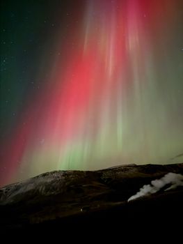 A stunning display of red and green auroras over a mountainous Icelandic terrain at night.