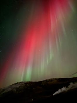 Vibrant aurora borealis illuminating Iceland's night sky with red and green hues.