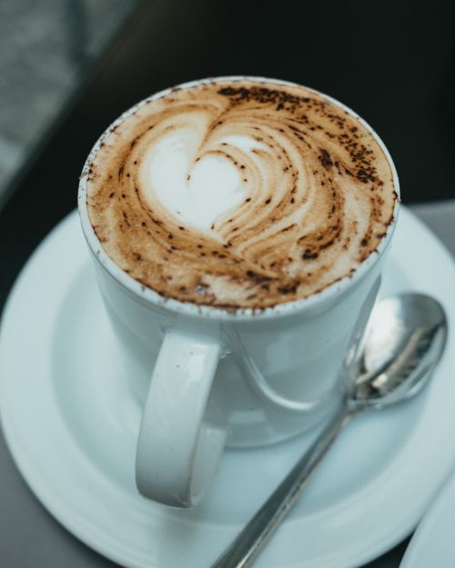 Free A close-up of a cappuccino with heart-shaped latte art, served in a classic Italian café setting. Stock Photo