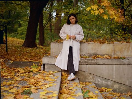 A woman in a coat in a leafy autumn park setting.