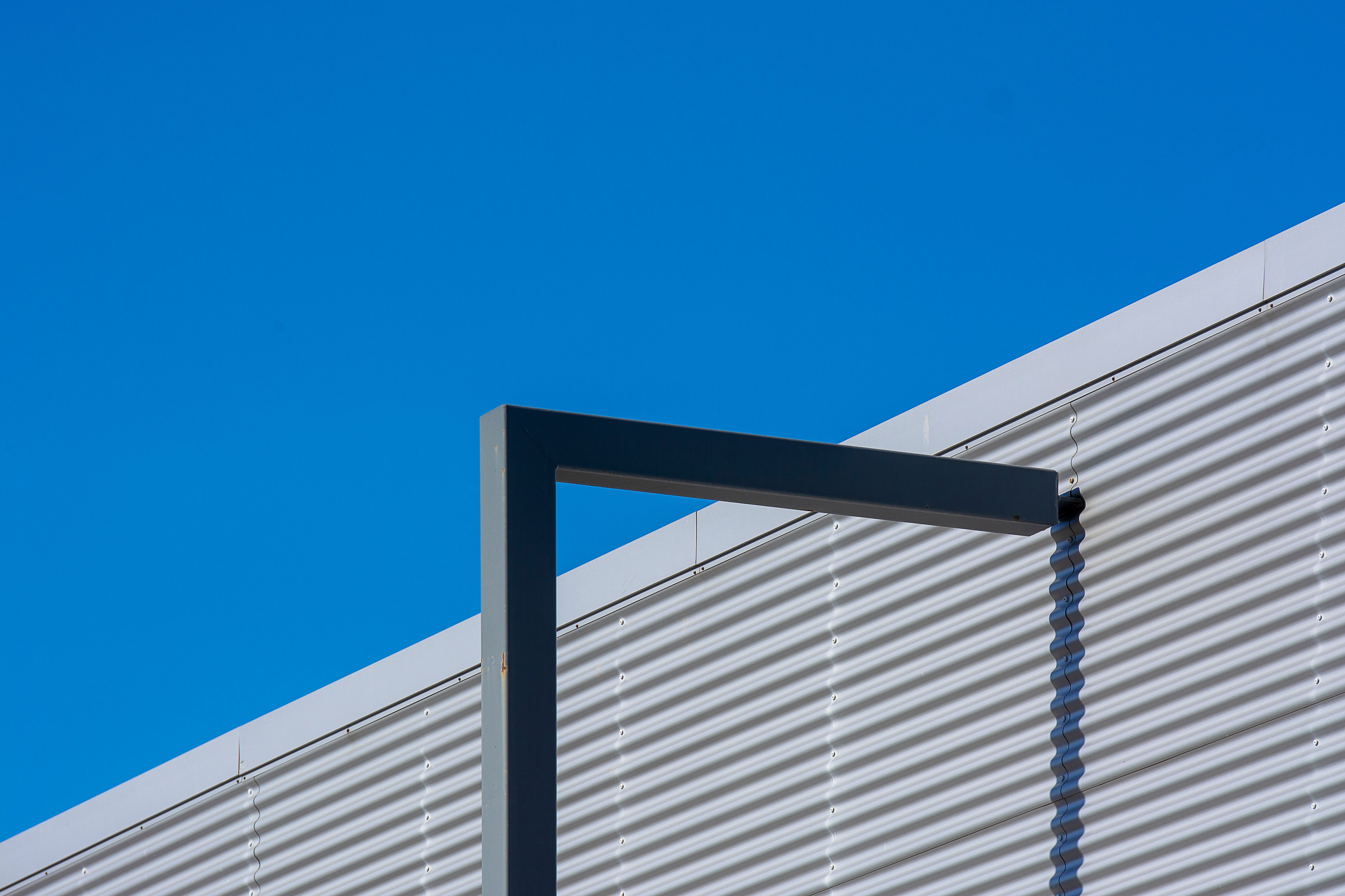 Détail architectural géométrique avec métal ondulé et ciel bleu clair, mettant en valeur un design moderne.
