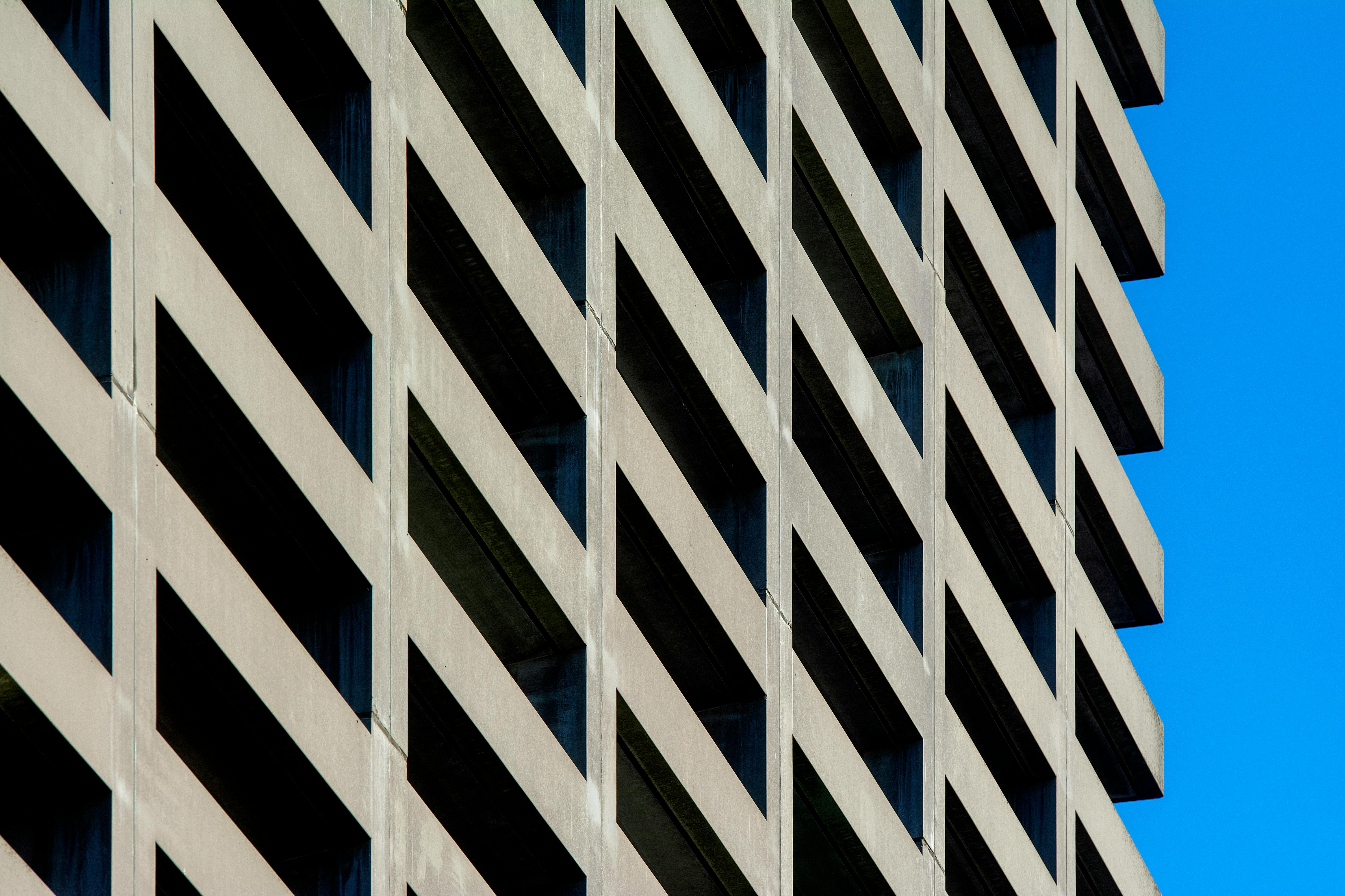 Kostnadsfria Närbild av en modern byggnadsfasad som lyfter fram kantiga linjer och geometriska mönster mot en blå himmel. Stock foto