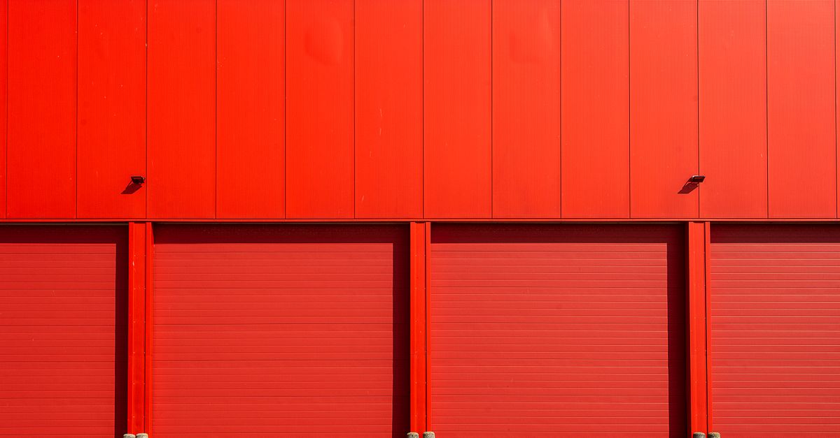Bright red industrial garage doors in a modern building facade under a clear blue sky.